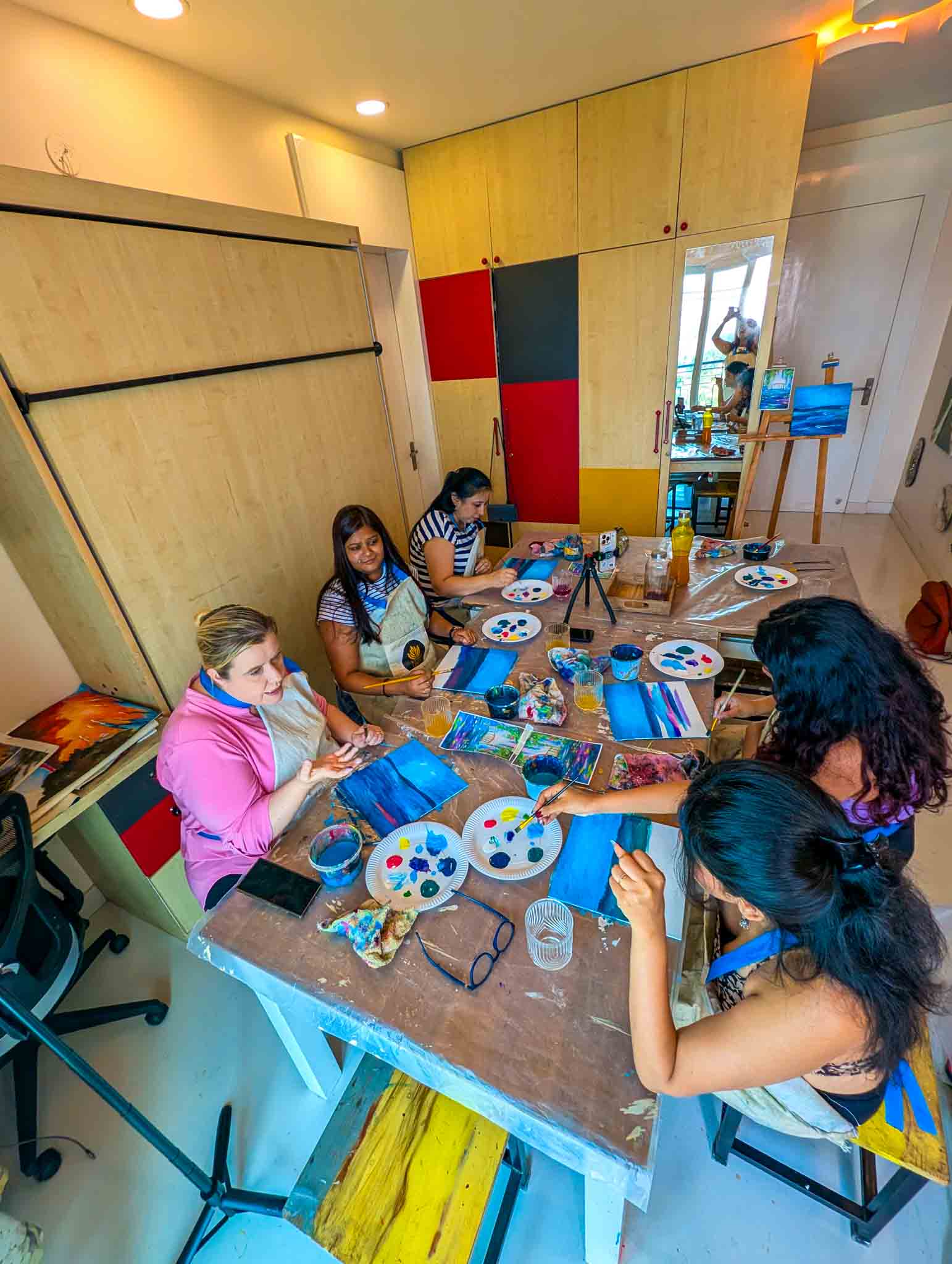 Cozy indoor setting with women happily painting blue-toned scenic canvases at a beginner-friendly Sip & Paint event.